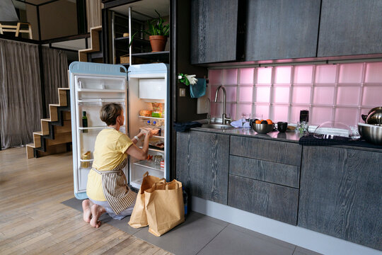 Woman stocking groceries in fridge at home