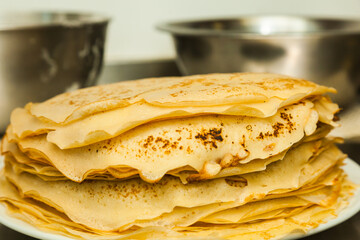 Ready pancakes are on the table, in a white plate, next to a stainless steel bowl on the table.