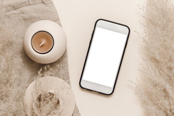 Mobile phone mockup with white screen with pampas grass and candles decoration, feminine home office desk, aesthetic mobile background. Smartphone template for design and branding