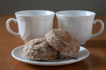 There are gingerbread cookies on the table. Behind are two white cups.