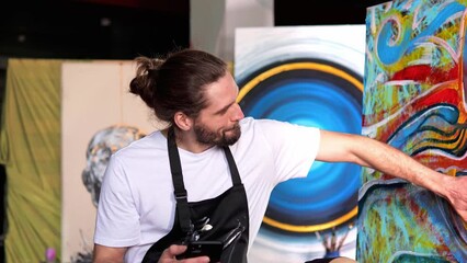 Successful artist with a satisfied expression is seen texting, having just sold one of impressive paintings online using mobile phone. Male feels proud and excited about the sale of artwork. Air kiss.