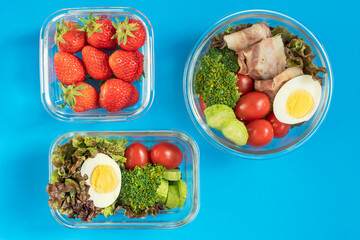 Healthy food in glass lunch boxes on blue background close-up, top view.
