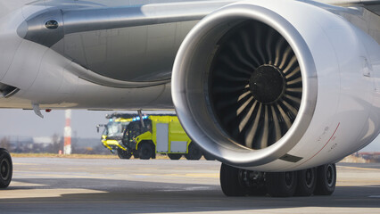 Fire truck of airport rescue and fire brigade behind engine of airplane on runway. Themes emergency...