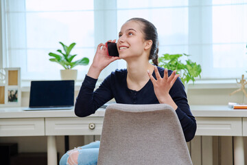 Cheerful teenage girl talking on phone at home