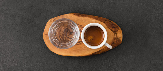 Cup of espresso coffee and glass of water on wood pad on dark table background. Speciality coffee...