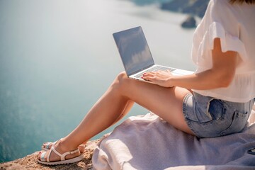Freelance women sea working on the computer. Good looking middle aged woman typing on a laptop keyboard outdoors with a beautiful sea view. The concept of remote work.