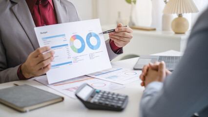 Two business people talking about report graph and analysis about finance budget or cost company and using calculator in office room.