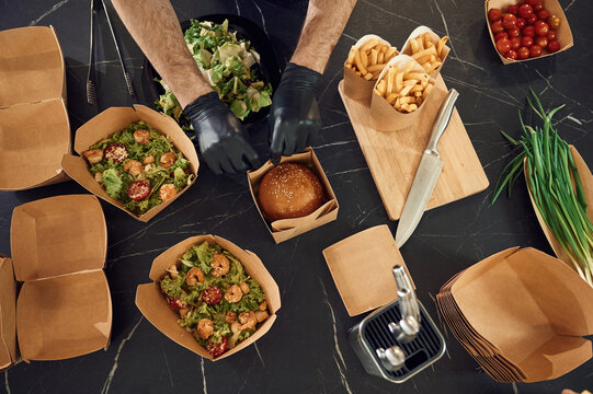 French fries, vegetables and burger. Man is packing food into the paper eco boxes. Indoors, restaurant