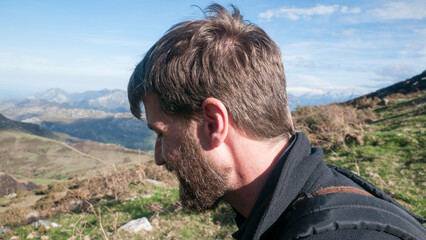 Hombre joven barbudo sentado  en ladera de montaña de Asturias