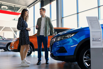A married couple at the dealership during the selection of a family car. A man and a young woman are looking at car options