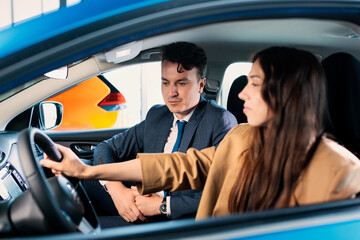 A sales manager tells a young woman about the new features of the car. A businesswoman in search of a new car