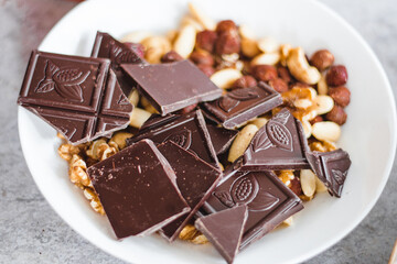 Chocolate with dried fruit, cashews, walnuts, hazelnuts in a white plate on the table, view from above, close up