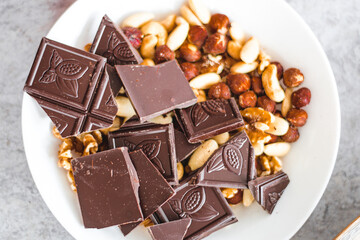 Chocolate with dried fruit, cashews, walnuts, hazelnuts in a white plate on the table, view from above, close up