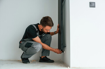 Plumber worker installing heating radiator in empty room of a newly built house