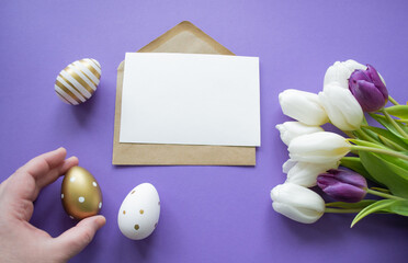 Easter greetings: close up hand holds golden egg, yellow tulips, painted white eggs on purple background