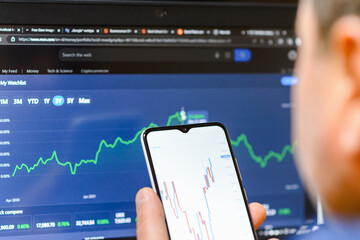 Trade and finance concept.Businessman checking stock market by his smartphone and laptop.Caucasian Male using mobile phone investing application.Stock market investment and trading app in hand.