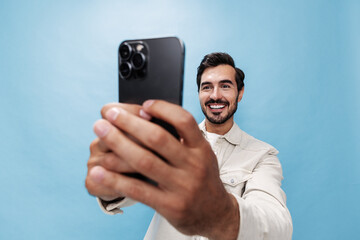 Portrait of a stylish man brunette smile with teeth and open mouth looking at the phone blogger with a beard taking selfies, on a blue background in a white T-shirt and jeans, copy space