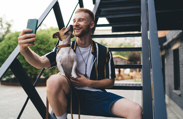 Cheerful male blogger with dog taking selfie on staircase