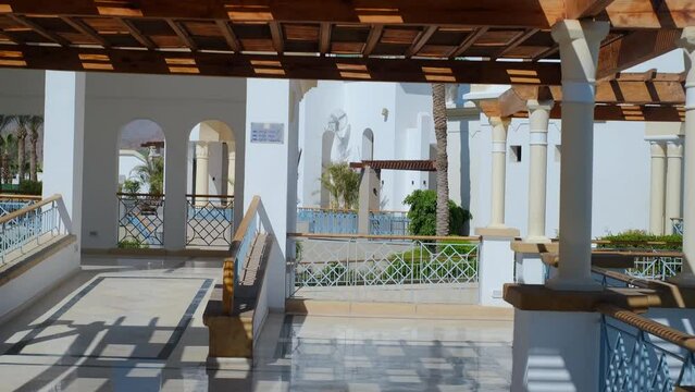 the wooden structure of the gazebo is supported by smooth cylindrical white columns sheltering the gazebo, the roof is clad in glass, connected to a retaining wall with a brick roof