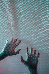 Nightmare horror. Emotional trap. Mental disorder. Defocused female hands clawing scratching transparent plastic bubble wrap textured wall free space background.