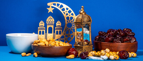 Ramadan muslim holiday background, with traditional treats - dates, nuts, dried fruits, sweets, religion rosary beads, lantern, tea, islamic Mosque, crescent moon Ramadan Kareem themed decorations