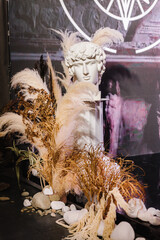 Gypsum statue of David's head. Classical sculpture plaster fragment of face of David. Dry leaves, grass and decor on photo zone. Clay modeling, sculpting workshops in studio. Ancient greek statue.