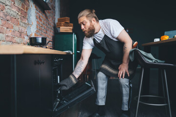 Fototapeta na wymiar Careful plump male putting baking sheet into stove