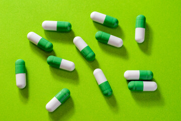 Scattered green and white capsules and pills on green background
