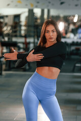 In the blue pants. Posing for a camera. Beautiful woman with sport body type is in the gym