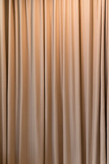 Beige curtain fabric texture and background. Large wall curtain. Curtain for hotel presentations. Cream colored cloth. Vertical photo.