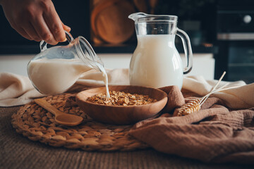 Aesthetic breakfast. Milk jug pouring milk into the bowl with natural muesli made from mix of unprocessed whole grains - obrazy, fototapety, plakaty