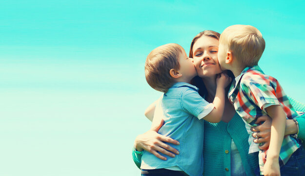 Family portrait, happy two children sons kissing their mom on a sunny day on blue sky background, Mothers day concept