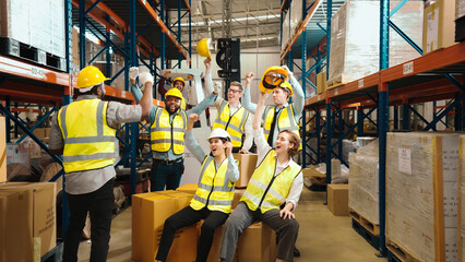 Multiracial warehouse workers in safety wear are dancing to relax after working hard on shipping goods. Male and female logistic employees are spending time together to celebrate the success of jobs.