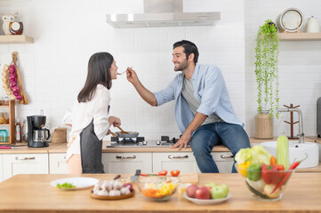 Happy young couple cooking together in the kitchen, feeding each other in their kitchen at home