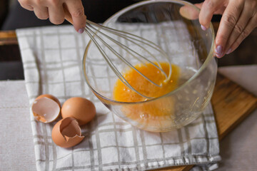 Elderly woman beats eggs with a wisk in a glass bowl. Prepare for making christmas pie or pancakes...