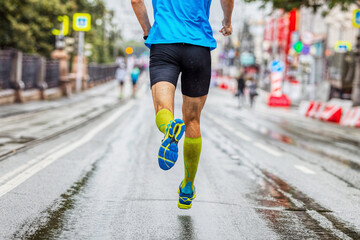 back male athlete in compression socks running marathon in city, summer sports race, jogging on wet...