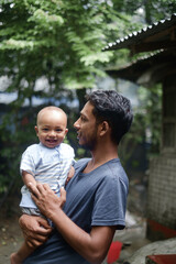South asian young rural father holding his little son, village baby boy playing with his young dad, lovely family moments in outdoor 