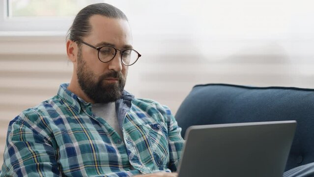 Serious male programmer typing on laptop at home, working remotely, freelancer