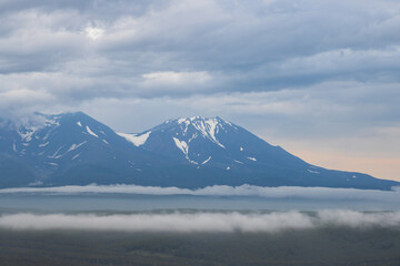 Naklejka na ściany i meble Beautiful evening landscape. View of the volcanoes. Overcast weather. Low clouds. Nature of the Kamchatka Peninsula. Travel and tourism in Siberia and the Russian Far East. Kamchatka Territory, Russia