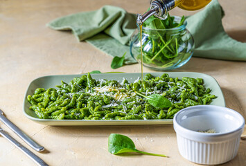Spinach spatzle (or green spatzle) are the typical Tyrolean green dumplings or gnocchi on plate with grated cheese. Olive oil pouring to the dish