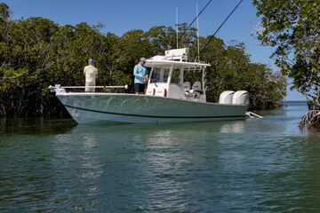 Fishermen on a center console boat next to mangrove trees.