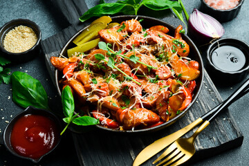 Fried potatoes with sausages and cheese, in a metal pan. On a dark background, close-up.
