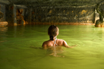 Fototapeta premium Girl kid child bathe swim in outdoor cave, dirty hot springs. Thermal water bath pool. Healthy natural clay. Yellow green mud. Spa wellness procedures, relax. Family winter vacation in mountain hotel