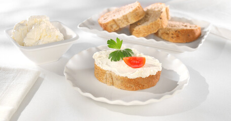slice of bread with cream cheese and tomato. bowl with creamy spread and sliced bread on a white tablecloth. healthy breakfast on a sunny day.