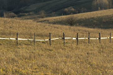 Fototapeta na wymiar Old wooden fence on yellow rural field in countryside in autumn nearby hill when sun goes down