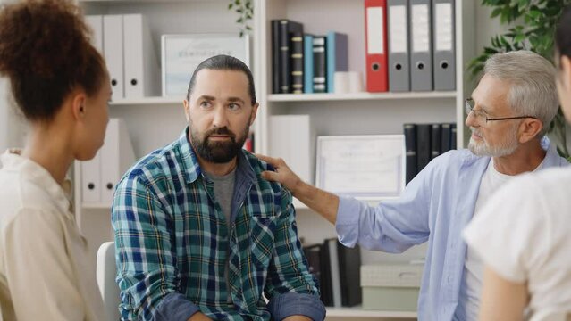 Diverse group of people comforting and supporting sad man at therapy session