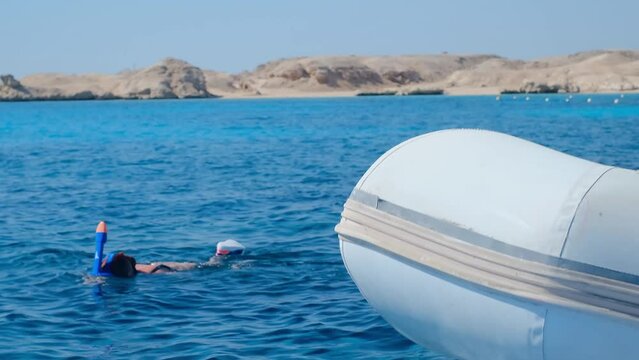 a girl in a mask snorkels in the sea, an inflatable boat is moored nearby, a sport, look at the fish in the sea, diving