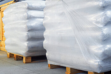 Storage of packaged goods or cargo in warehouse. On wooden pallets there are bags of cement wrapped...