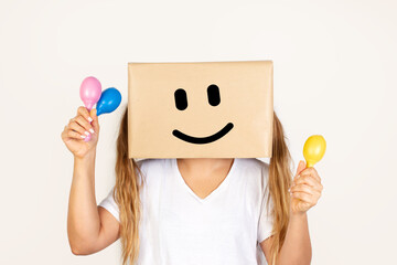 Mujer sonriente con una caja de cartón en la cabeza sosteniendo unas maracas de colores sobre un fondo blanco liso y aislado. Vista de frente y de cerca. Copy space
 - obrazy, fototapety, plakaty