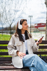 One young girl is listening to music on her wireless headphones and using her phone outdoors